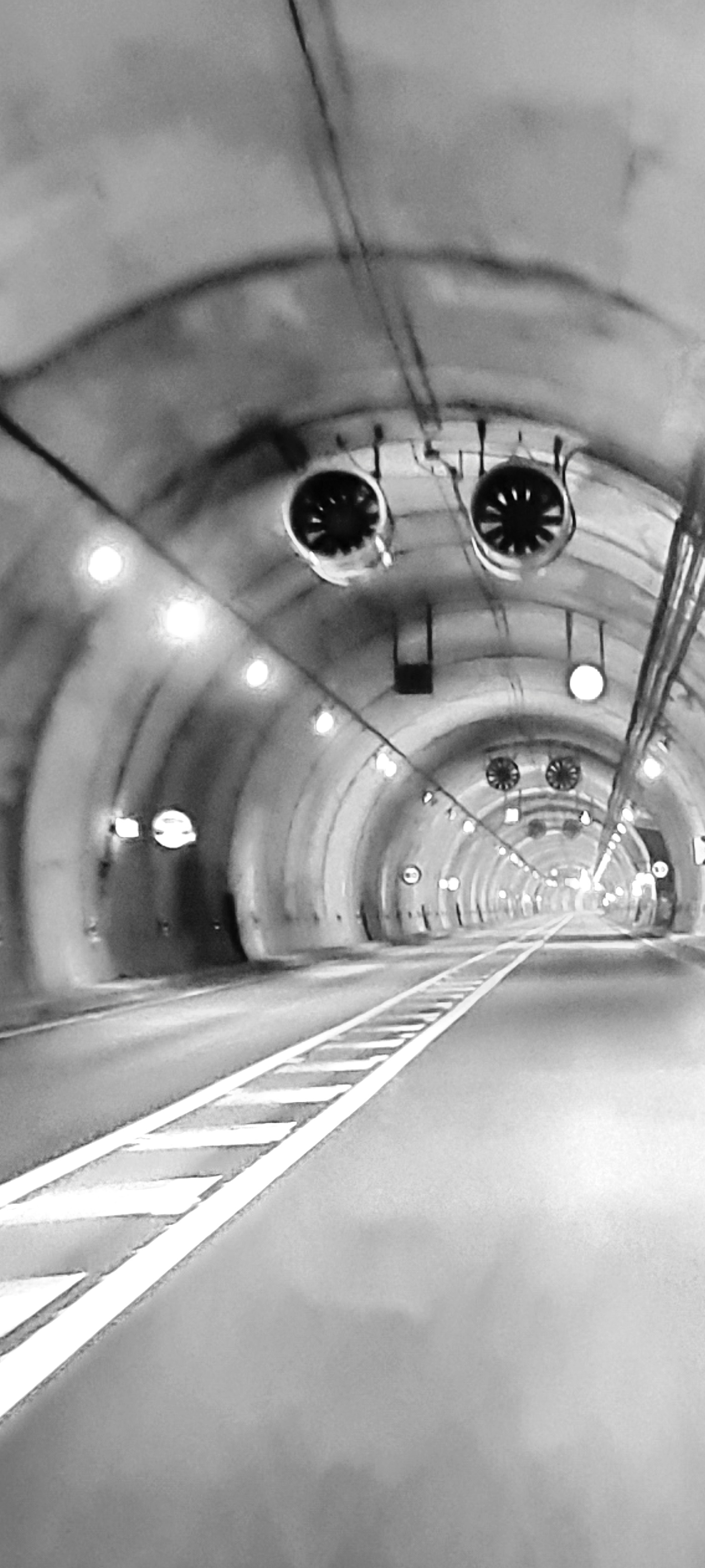 Túnel vacío en blanco y negro, con luces circulares en el techo y una vía lateral.
